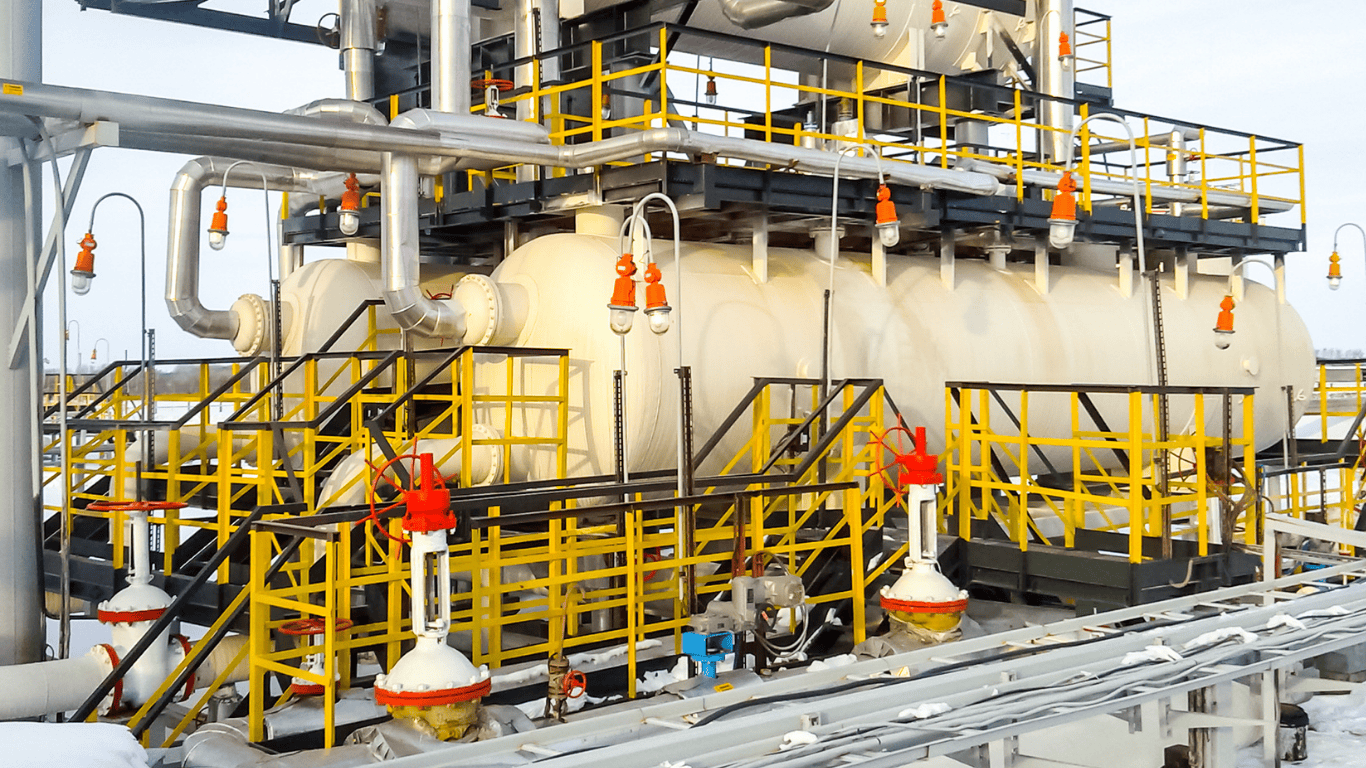 An industrial facility with large cylindrical tanks, metal pipes, insulated lines, railings, and bright yellow safety platforms, shown outdoors in winter conditions, illustrating the complexity of plumbing systems and how proper drain maintenance prevents issues inside and outside buildings. Although the image shows heavy equipment rather than a home sink drain, it represents how clogs can form anywhere—from large tanks and traps in commercial plumbing to residential tubs, toilets, and floor drains—when debris like paper towels, coffee grounds, hair, or grease enters the drain system. A homeowner trying to unclog a drain might pour boiling water, use baking soda and vinegar as a natural solution, fill a cup, bucket, pan, or pot with hot water, or grab a plunger, drain cleaner, liquid drain product, snake, or other tools to avoid calling a plumber. For properties with septic tanks, using gentle methods like baking soda, vinegar, and avoiding harsh chemicals protects the beneficial bacteria that keep the system functioning. Whether fixing a small clog forming in a kitchen pipe or maintaining large industrial plumbing shown here, keeping drains clean prevents bad smell, protects walls and floors from leaks, and avoids buildup forming deep inside the system. Proper use of a stick to clear simple debris, replacing a cover, or choosing the right tool helps ensure effective fixing without damage.