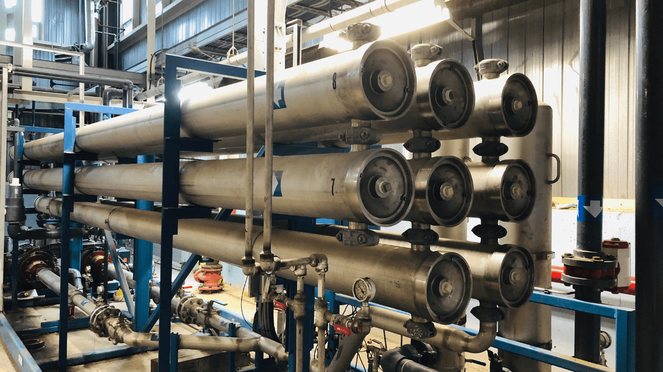 Industrial reverse osmosis system shown inside a water treatment facility, featuring stainless-steel pressure vessels and piping used in a commercial reverse osmosis system designed for removing impurities from water. The reverse osmosis system represents advanced RO systems and an osmosis system commonly used in commercial applications and water treatment facilities across various industries, including food and beverage sectors that require fresh water and solutions tailored to specific needs. This commercial RO system integrates other filtration techniques such as carbon block filtration to reduce contaminants and bacteria, providing a full line of treatment options for seawater or other challenging sources. The image highlights how commercial systems and osmosis technology support water treatment processes that help companies save money while ensuring reliable filtration, efficient treatment, and dependable performance. A quick view of the equipment shows its industrial design optimized for commercial operations and high-quality water production.