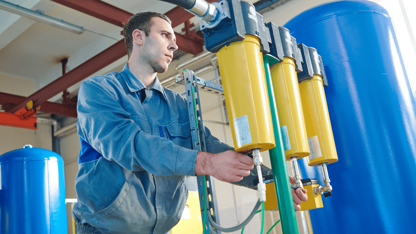 A technician adjusts yellow membrane filtration housings inside an industrial water treatment facility containing large blue pressure vessels and interconnected piping. The scene illustrates membrane treatment systems including RO systems, UF systems, and NF systems used for water reuse and high-purity water production, representative of ProChem Water technologies.