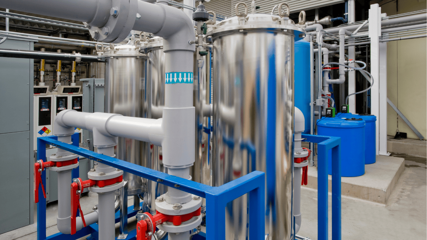 A close-up view of a wastewater treatment facility featuring stainless steel filtration units, pipes, valves, and blue storage tanks. The setup is part of an industrial water reuse system, designed for wastewater recycling and water recovery. The equipment is part of a modular reuse plant designed to efficiently treat and reuse wastewater, showcasing the technology behind ProChem Water's wastewater reuse systems and equipment.