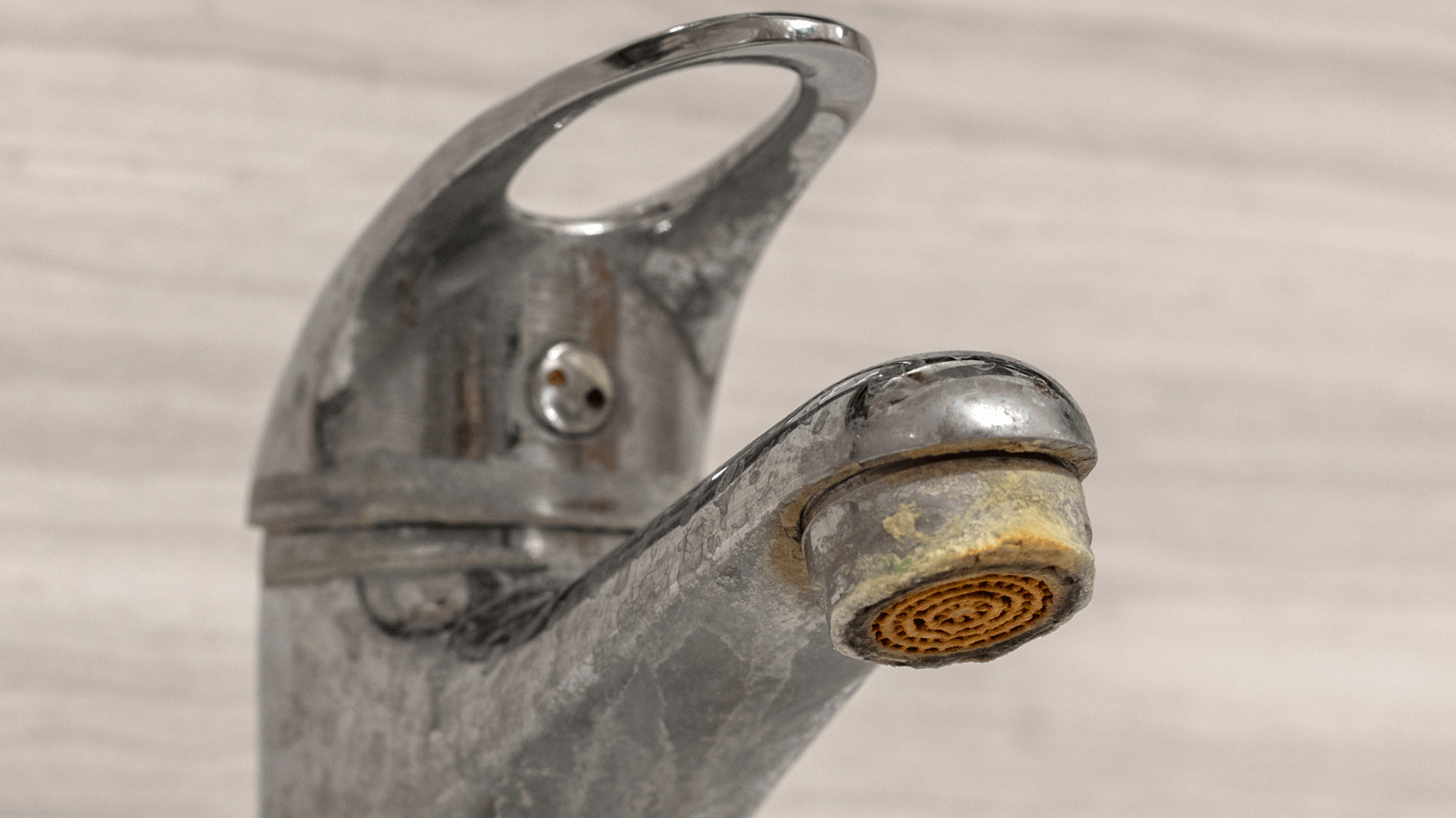 Faucet with visible hard water build up and calcium deposits, showing mineral buildup, limescale, and soap scum around the aerator. The image illustrates how to remove hard water build up on metal fixtures caused by dissolved minerals like calcium carbonate and magnesium. Common in industrial water systems, this buildup reduces water flow and efficiency, requiring cleaning solutions such as vinegar and baking soda or professional descaling methods.